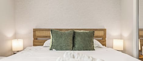 Una cama bien hecha con almohadones verdes, un cabecero de madera y dos lámparas de noche.