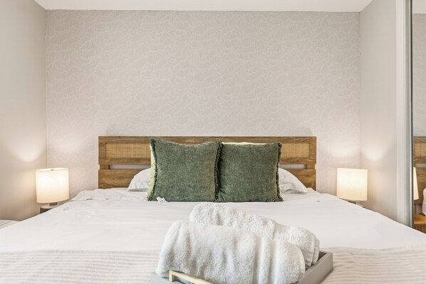 Una cama bien hecha con almohadones verdes, un cabecero de madera y dos lámparas de noche.