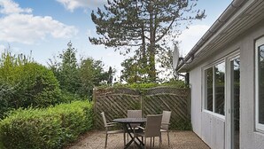Une terrasse extérieure avec une table et des chaises, entourée d’une clôture en bois et d’une végétation luxuriante.
