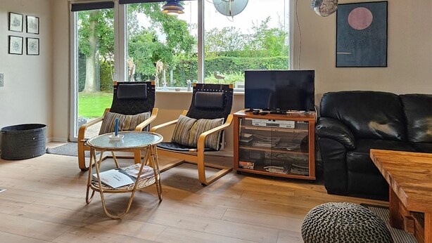 Un salon avec un canapé en cuir noir, deux fauteuils, une table basse en verre et un meuble pour la télévision avec un téléviseur à écran plat.