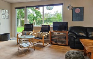 Un salon avec un canapé en cuir noir, deux fauteuils, une table basse en verre et un meuble pour la télévision avec un téléviseur à écran plat.