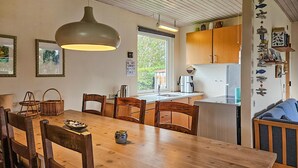 Une cuisine chaleureuse avec des meubles en bois, une table à manger avec des chaises, un luminaire suspendu et une fenêtre laissant entrer la lumière naturelle.