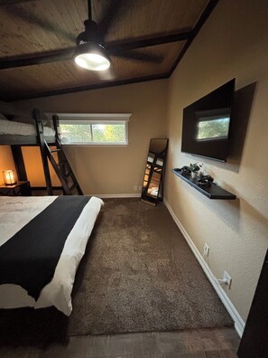 Quarto com cama beliche, janela, espelho, televisão e prateleira com plantas.