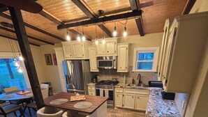 A kitchen with wooden cabinets, a stainless steel refrigerator, a microwave, and a stove. There is a dining table with two chairs.