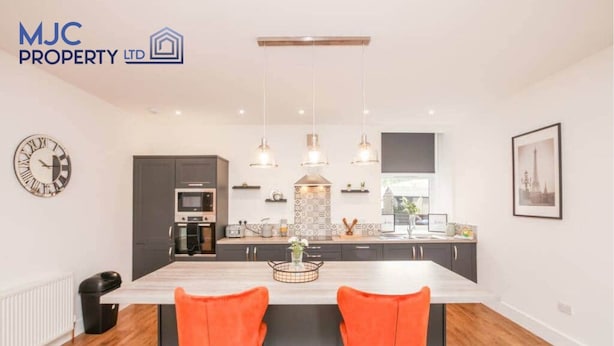 A modern kitchen with a central island, pendant lights, and a dining area with two orange chairs. - Mansfield - sleeps 8 guests  in 3 bedrooms (Hawick)