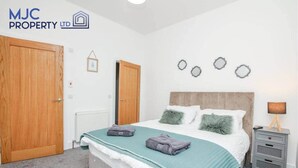 A bedroom with a bed, two doors, a bedside table, and wall decorations. - Mansfield - sleeps 8 guests  in 3 bedrooms (Hawick)