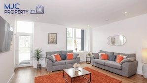 A spacious living room with two grey sofas, a coffee table, and a red rug. - Mansfield - sleeps 8 guests  in 3 bedrooms (Hawick)
