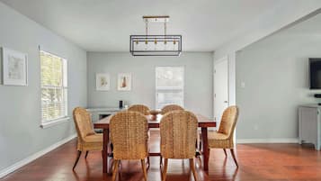 A dining room with a wooden table and wicker chairs, a chandelier, and framed artwork on the walls.