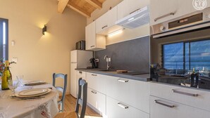 A modern kitchen with a dining area, featuring a built-in oven, a microwave, and a large window offering a view. - LE ZERBLET - ORELLE - Gîte (ORELLE)