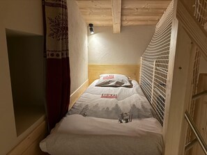 A small, narrow room with a wooden ceiling and a single bed with a white bedspread featuring a mountain scene. - LE ZERBLET - ORELLE - Gîte (ORELLE)