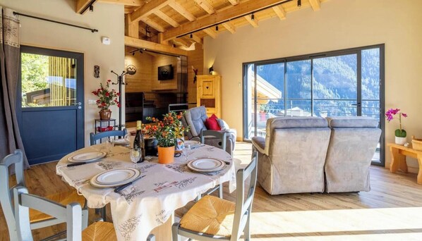 Un coin repas avec une table dressée pour deux personnes, un canapé et une vue sur les montagnes.