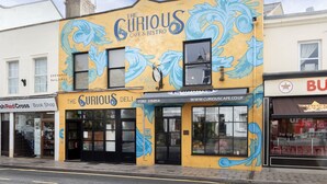 A building with a mural of blue waves and the text "The Curious Cafe & Bistro".