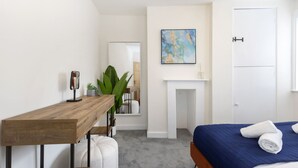 Ein Schlafzimmer mit einem Holztisch, einem Bett mit blauer Bettdecke, einer weißen Tür und einem Gemälde an der Wand.