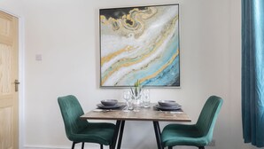 A dining area with a marble artwork, two green upholstered chairs, a wooden table, and a blue curtain.