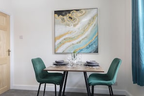Ein Essbereich mit einem Marmorbild, zwei grünen Polsterstühlen, einem Holztisch und einem blauen Vorhang.