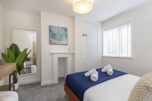 Ein Schlafzimmer mit Bett, Spiegel, Kamin, einem Fenster mit Jalousien und einer Pflanze.
