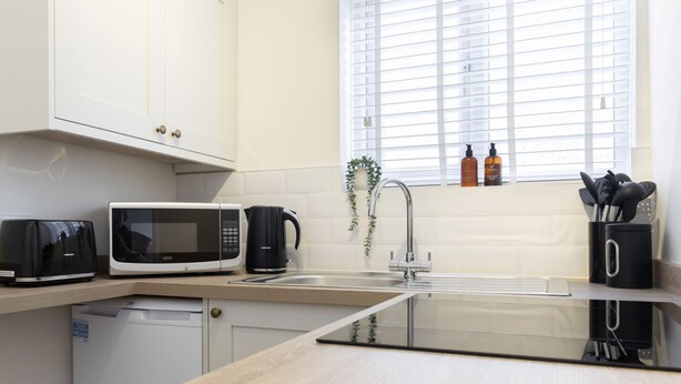 A modern kitchen with a dishwasher, microwave, kettle, and sink.