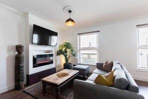 A living room with a flat-screen TV, a fireplace, a coffee table, a sofa, and a potted plant.
