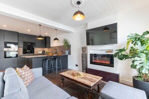 A modern living room with a grey sofa, a wooden coffee table, and a fireplace. - Central 2-Bed Modern Home with Garage (Cheltenham)