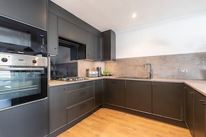 A modern kitchen with dark cabinetry, a built-in oven, a microwave, and a stainless steel range hood.