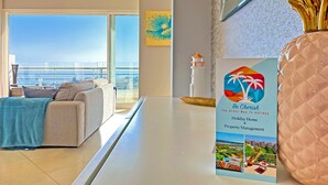 Ein modernes Wohnzimmer mit einer Couch, einem großen Fenster mit Meerblick und einem Schild für die Immobilienverwaltung 'Be Cherish The Other Way To Holiday'.