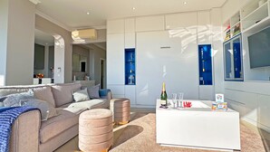 Ein modernes Wohnzimmer mit einer Couch, Hocker, einem Couchtisch und einem Fernseher.