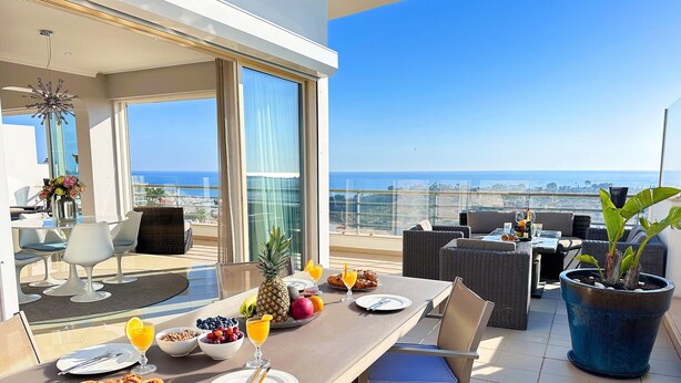 Ein Balkon mit Esstisch, gedeckt für ein Frühstück, mit Blick auf das Meer.