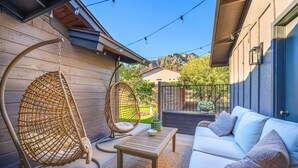 Eine Terrasse mit einer weißen Couch, zwei Korbstühlen, einem kleinen Tisch und einem Hängesessel.