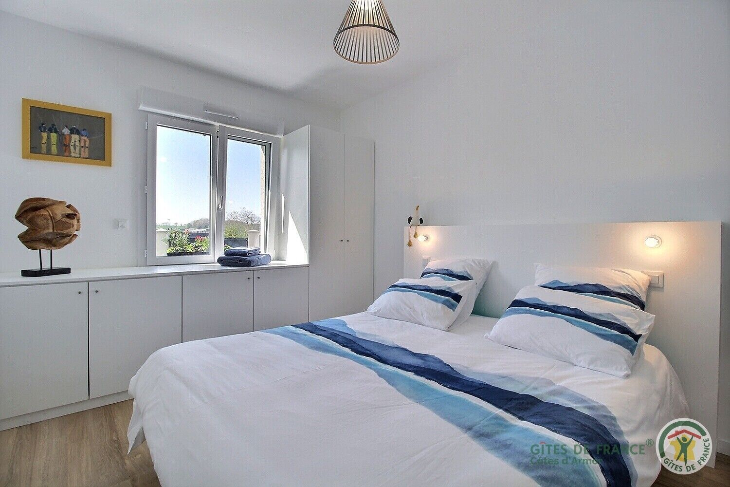 A bedroom with a large bed, a window with a view, and a ceiling light fixture.