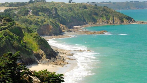 Un paysage côtier avec une plage, des falaises et une vue dégagée sur l’océan.
