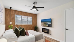 Un dormitorio con cama, ventilador de techo, televisión y chimenea.