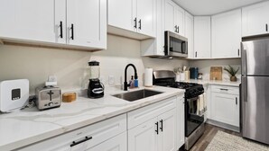 Una cocina moderna con armarios blancos, un refrigerador de acero inoxidable, un microondas, una estufa y un lavamanos.