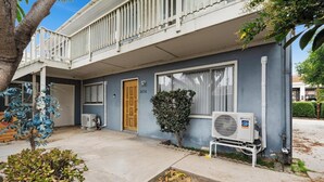 Un edificio de dos pisos con un balcón, una puerta de madera y una ventana con marco blanco.