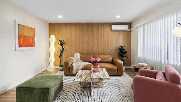 Una sala de estar moderna con un sofá de cuero marrón, un reposapiés verde, una mesa de centro de mármol y un sillón rosa.