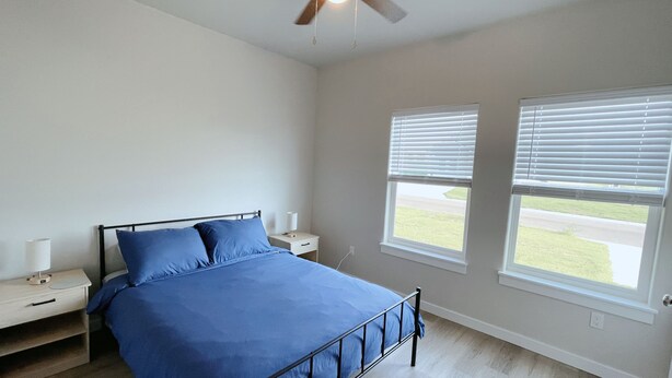 A bedroom with a bed, two bedside tables, a ceiling fan, and two windows with blinds. - 10 min to Casino, brand new 2b/1b single home 2025 (Durant)
