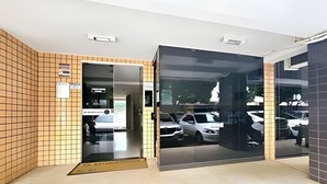 Entrada de un edificio moderno con un muro de azulejos, puerta de cristal y vista a coches estacionados afuera.