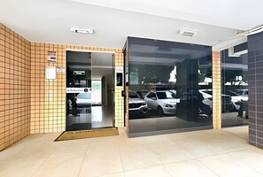 Ein moderner Hauseingang mit einer Kachelwand, einer Glastür und Blick auf geparkte Autos.