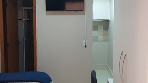 Un dormitorio con cama, armario, una mesita y televisor en la pared.