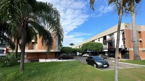 Un edificio con techo plano, estacionamiento y zona verde con palmeras.