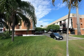 Ein Gebäude mit flachem Dach, Parkplatz und einer Rasenfläche mit Palmen.