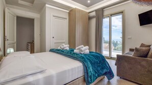 A modern bedroom with a large bed, a view of the outdoors, a sofa, and a TV mounted on the wall. - Amazing home in Trabia (Trabia)