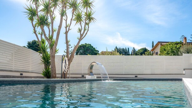 A swimming pool with a water feature, palm trees, and a white fence. - Amazing home in Trabia (Trabia)