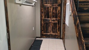 Un pasillo con una puerta de madera, un estante blanco con texto árabe y un felpudo negro en el suelo.