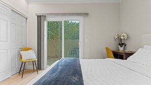 Een slaapkamer met een bed, een gele stoel, een bureau met een bloevas, en een schuifdeur naar buiten.