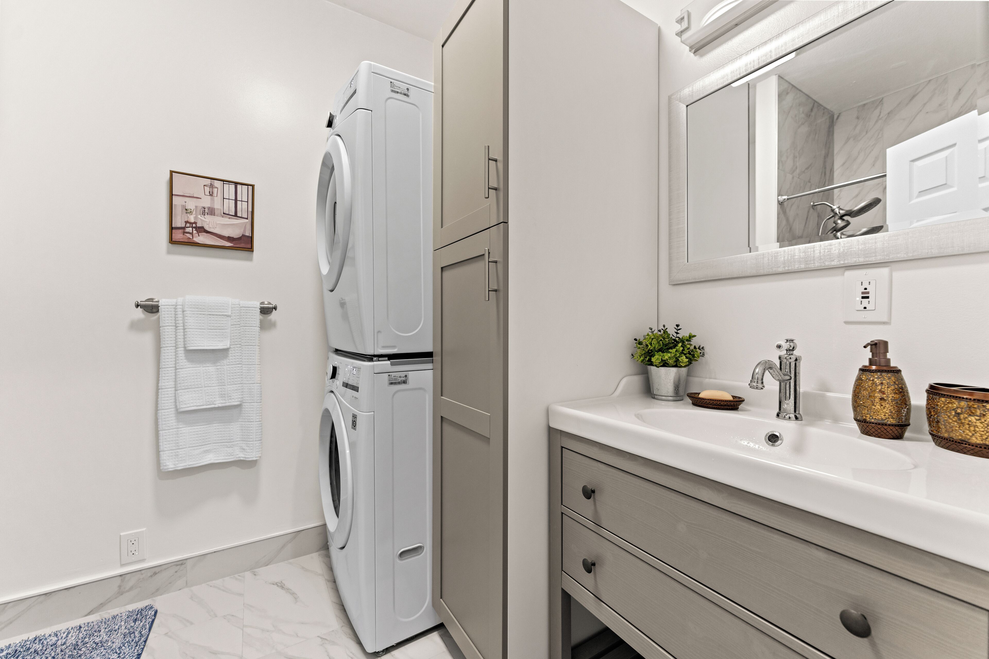 A modern bathroom with a stacked washer and dryer, a sink with a mirror, and a towel rack.