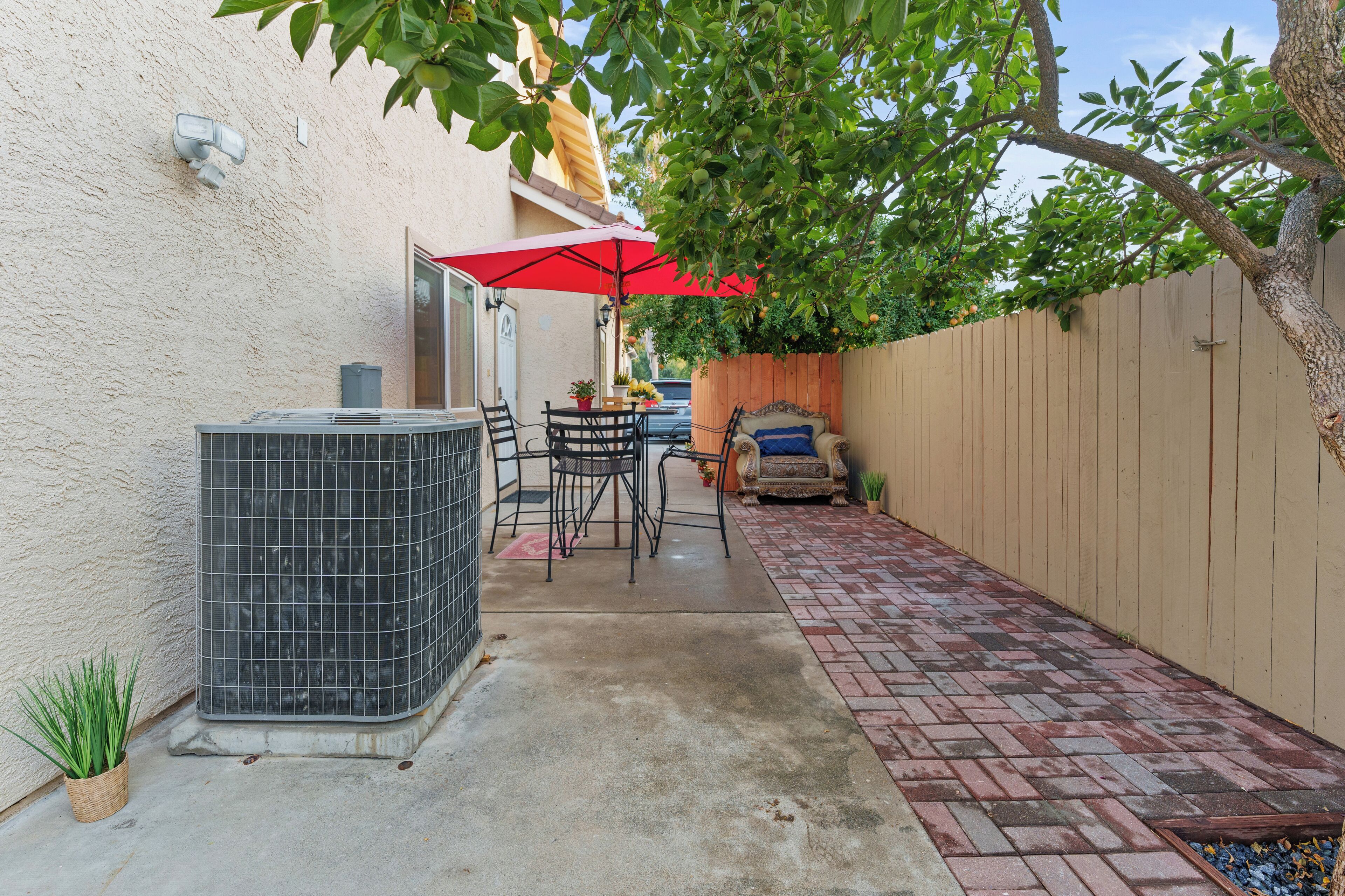 A patio area with a tiled floor, a table with chairs, a red umbrella, and a potted plant.