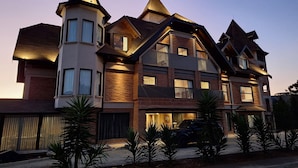 A multi-story house with a prominent tower, multiple balconies, and a driveway with parked vehicles. - Château Suisse Boutique Hotel (Campos do Jordão)