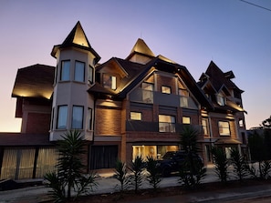 A multi-story house with a prominent tower, multiple balconies, and a driveway with parked vehicles. - Château Suisse Boutique Hotel (Campos do Jordão)