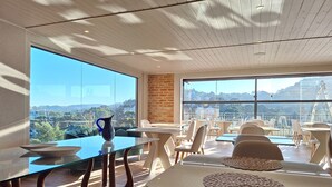 A modern dining area with a glass table, chairs, and a view of a cityscape through large windows. - Château Suisse Boutique Hotel (Campos do Jordão)