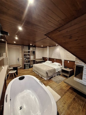 Une chambre avec une grande baignoire, un lit avec une literie blanche, un plafond en bois et un petit bureau avec une chaise.